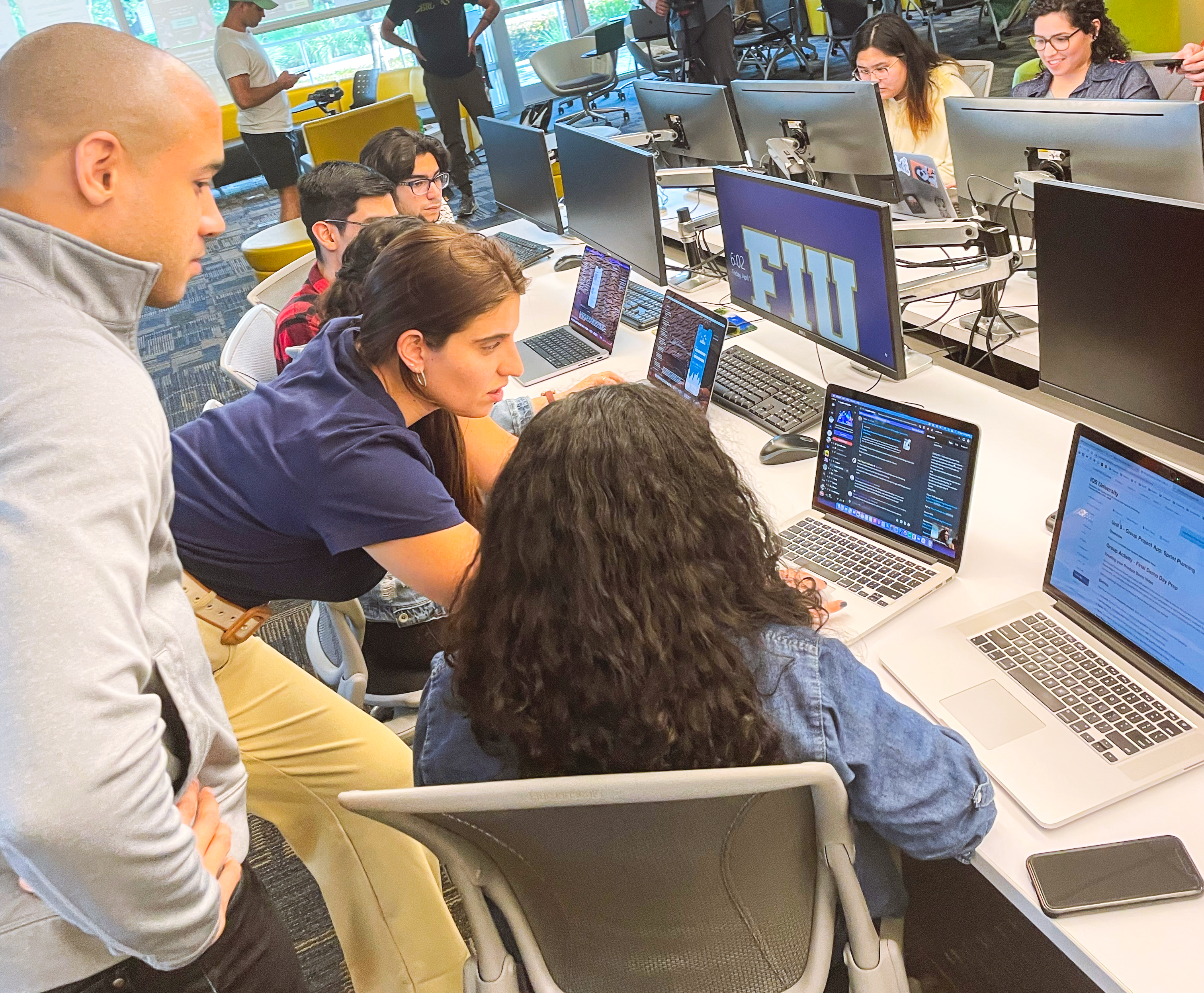 Group of students huddled around a desk with laptops